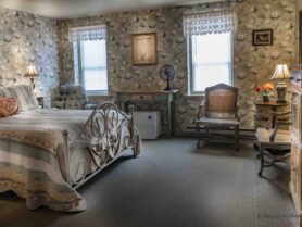 room with floral wallpaper, bed, rocker, recliner