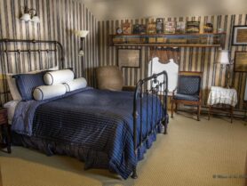 bedroom with iron bed with blue bedspread, 2 chairs