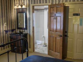 iron bed with blue bedspread, looking into bathroom