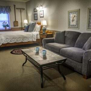 bed with white bedspread, sofa and coffee table with 2 mugs